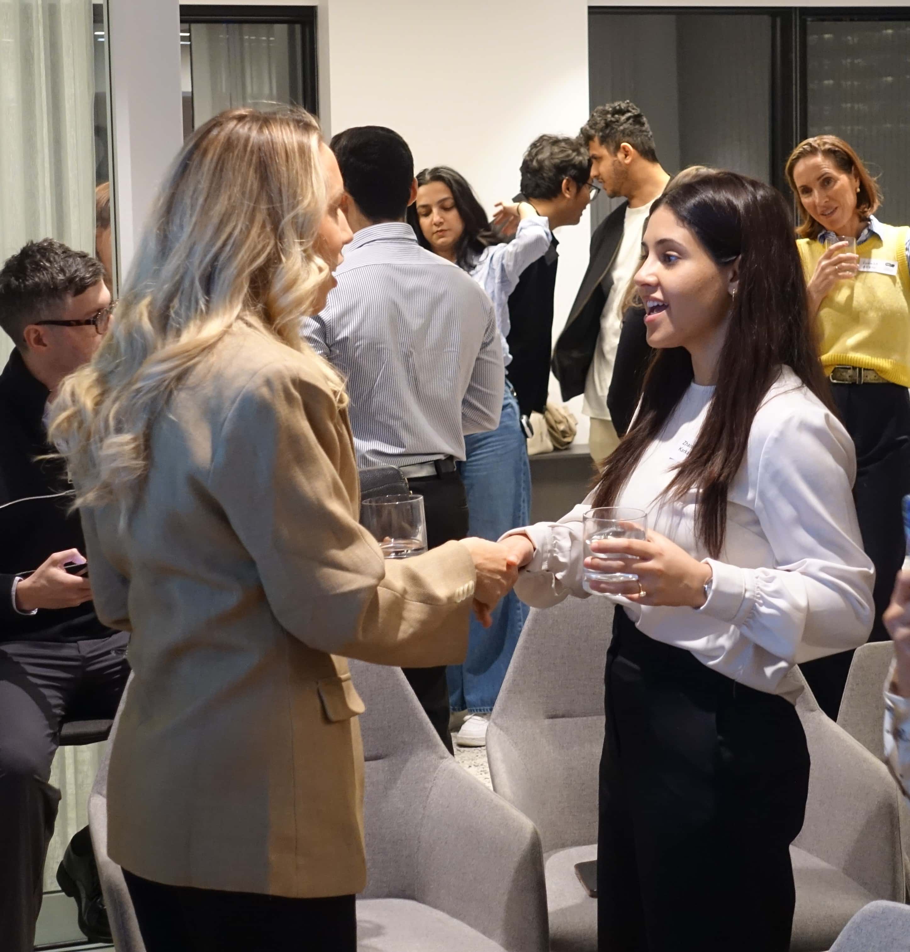 Two people speaking and shaking hands in a crowded room