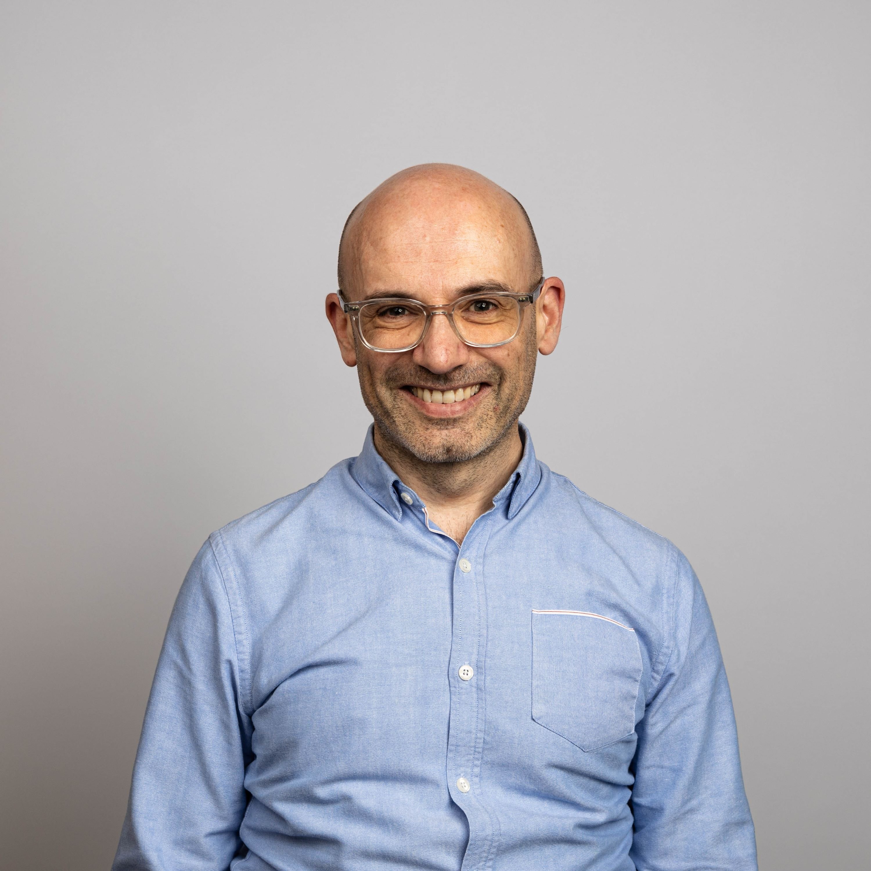 Portrait style photo of Michael Apte,  wearing blue shirt and glasses.